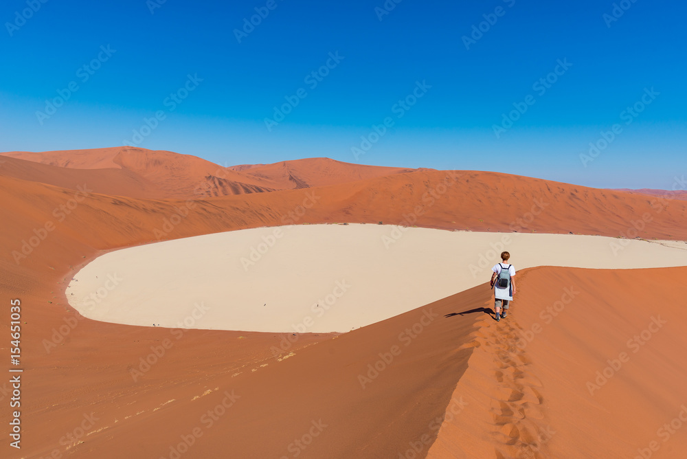Tourist walking on the scenic dunes of Sossusvlei, Namib desert, Namib Naukluft National Park, Namibia. Adventure and exploration in Africa. Tourist walking on the scenic dunes of Sossusvlei, Namib desert, Namib Naukluft National Park, Namibia. Adventure and exploration in Africa.
