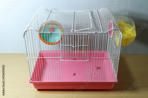 old and empty white and pink hamster cage on wood desk with hamster wheel and yellow hamster toilet