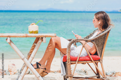 Young sexy woman with earphones using phone on the beach