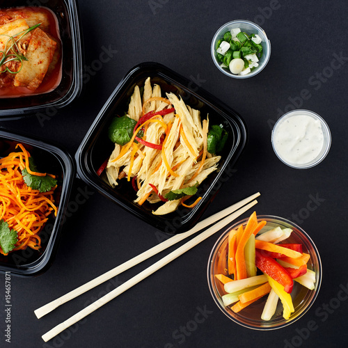 Korean cuisine. Set of salads on black background. Asparagus, korean carrot, kaktugi, fresh vegetable sticks and green onion. photo