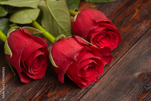 Three beautiful red roses on wooden table  romantic background