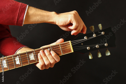 Hands of guitarist tunes the guitar on a dark background photo