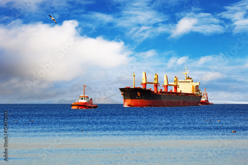 Tugboats towing a large cargo ship on sea.