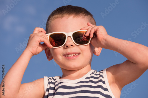 happy smiling little boy wearing sunglasses with ocean sunset reflection