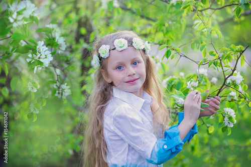 Adorable little girl in blooming apple tree garden on beautiful spring day. Cute child picking fresh apple tree flowers at sprin
