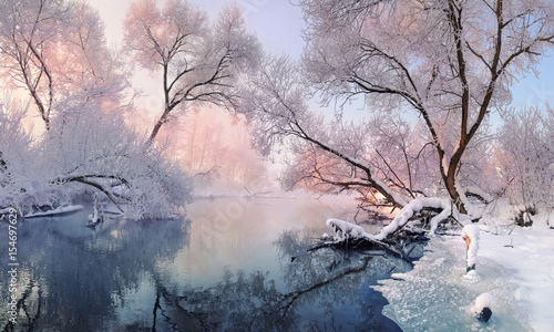 Сhristmas Lace.Winter landscape in pink tones with hoarfrost everywhere.Mostly calm winter river, surrounded by trees covered with hoarfrost and snow that falls on a beautiful pink morning light. 