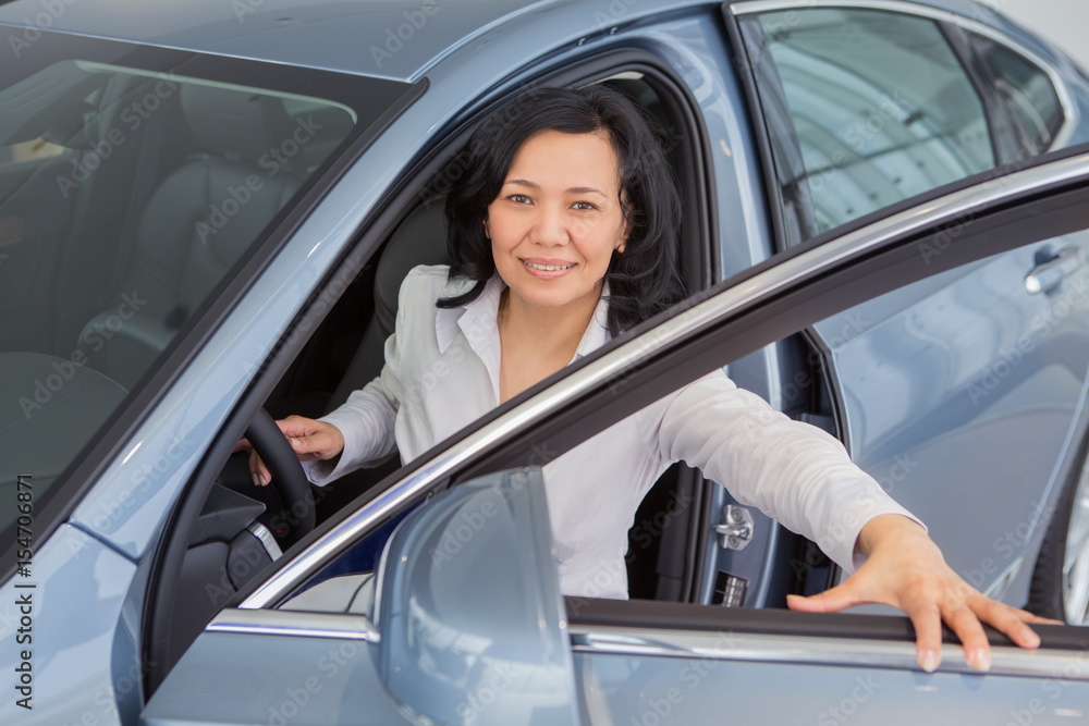 Beautiful mature woman checking out new cars at the dealership