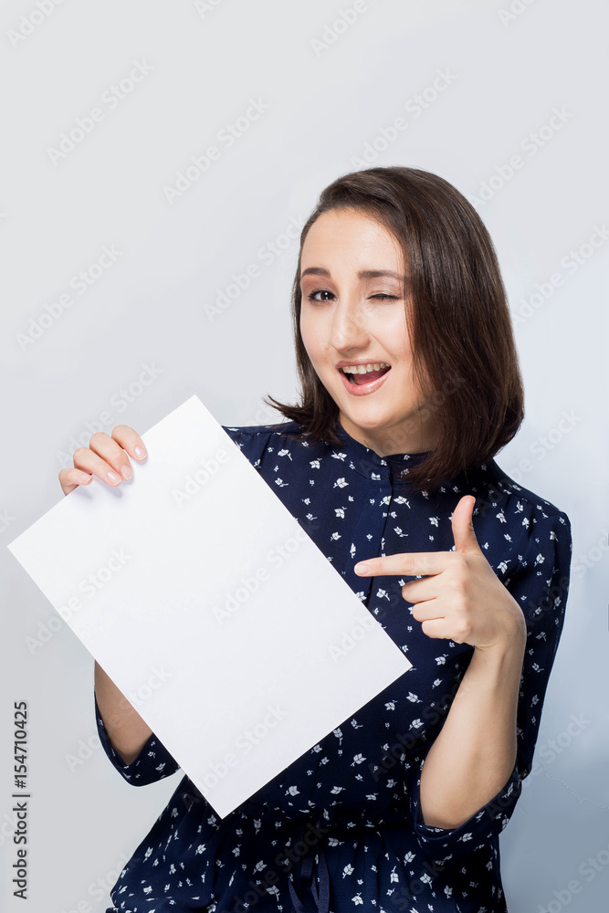 Naklejka premium beautiful brunette girl shows a finger on a clean white paper, winks with a smile, happiness, joy, emotions