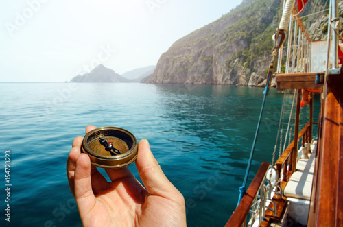 Hand holding old compass on wooden boat in the sea photo