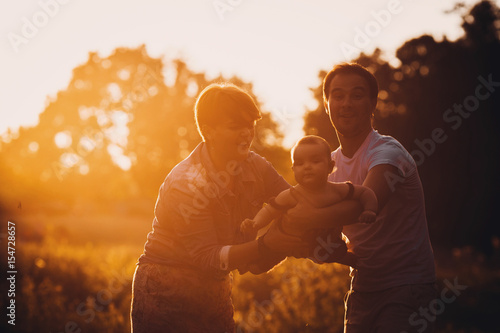 Parents hold their little daughter like an airplane standing in the rays of golden sun