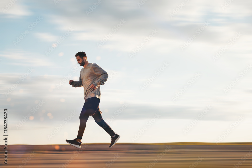 Young athlete in headphones and sports clothes and sneakers runs in the park. Lubricated background. Motion blur Young athlete in headphones and sports clothes and sneakers runs in the park. Lubricated background. Motion blur