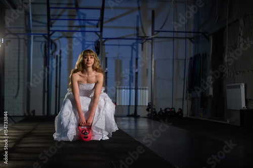 Beautiful and muscular blonde bride in a wedding dress doing exercise with weight, Crossfit photo