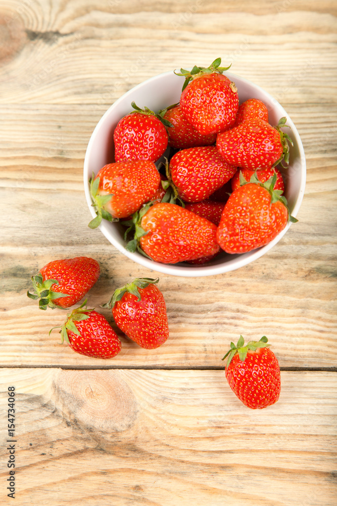 Ripe strawberry in a white bowl on a wooden background