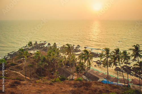 Palm trees in the rays of the sunset in the background rocks and the Arabian Sea