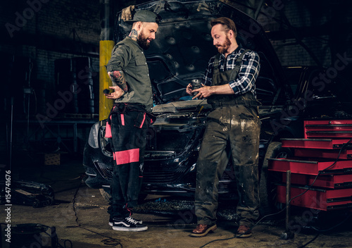 Two bearded mechanics inspecting car's engine parts.