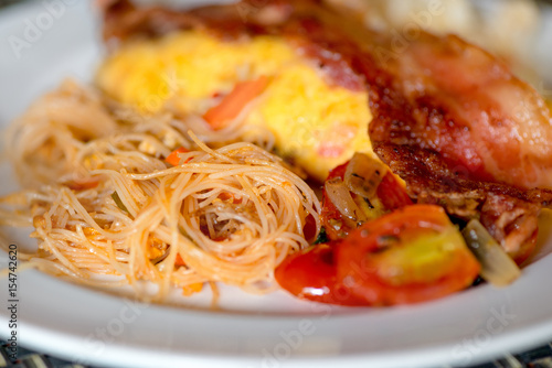 Asian dish - fried noodles with egg, tomato and bacon close-up on a plate