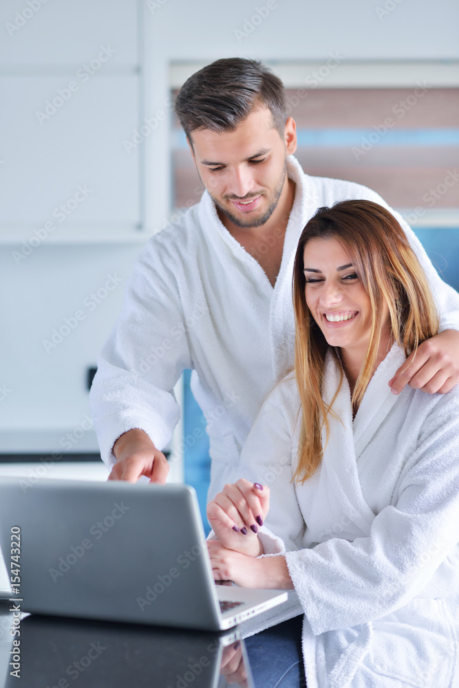young couple in bathrobe at home having coffee in the kitchen and working on laptop computer young couple in bathrobe at home having coffee in the kitchen and working on laptop computer