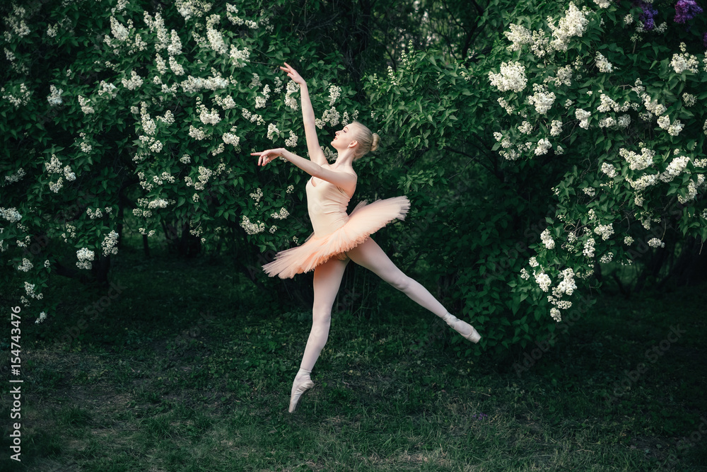 Young woman in white tutu dancing in the green flowers landscape. Beautiful ballerina showing classic ballet poses and jumping high into the air. Concept of female tenderness and harmony life.