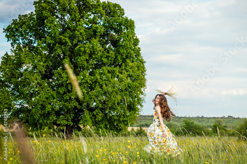 beautiful young free girl in light dress with lemons and bouquet of wildflowers, in the middle of a spacious field with a large tree in the middle of it, with sky and clouds on sunny day. 