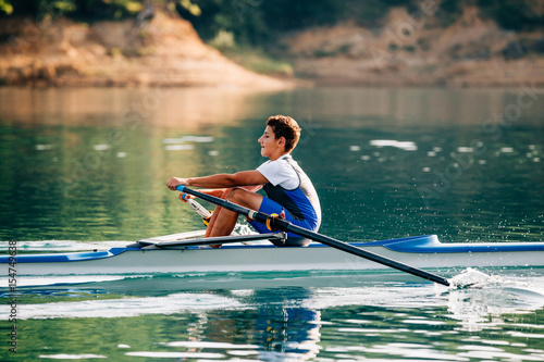 A Young single scull rowing competitor paddles on the tranquil lake