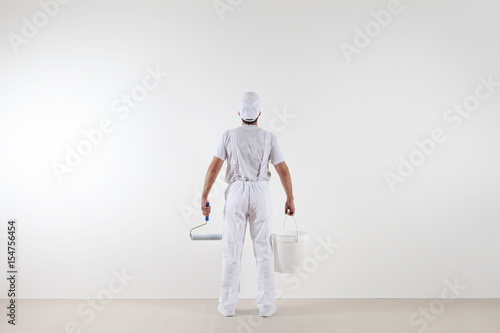 Rear view of painter man looking at blank wall, with paint roller and bucket, isolated on white room photo
