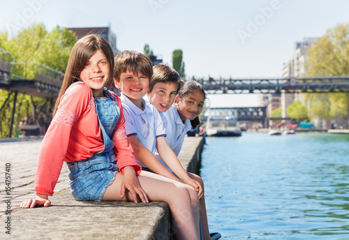 Four happy friends sitting in a line on embankment