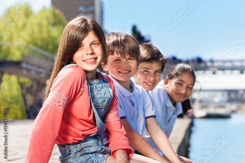 Four friends sitting in a line on bank of river