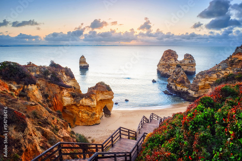 beautiful Atlantic ocean view horizon with sandy beach,  rocks and waves at sunrise. Algarve,  Portugal