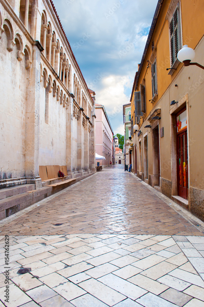 Cozy and empty narrow street between two stone houses on a summer morning. Dramatic cloudy sky. Zadar center, Croatia