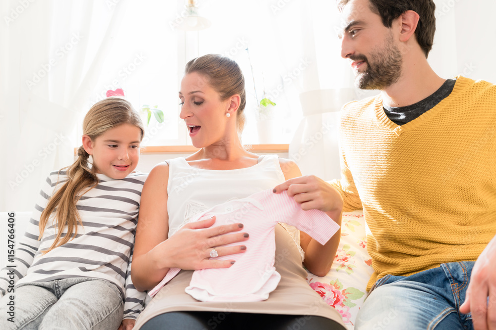 Mother, father and daughter awaiting family addition and looking at baby clothes Mother, father and daughter awaiting family addition and looking at baby clothes