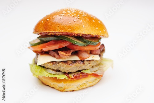 Appetizing burger with chop, bacon, bacon, cucumber, greens, salad on white background