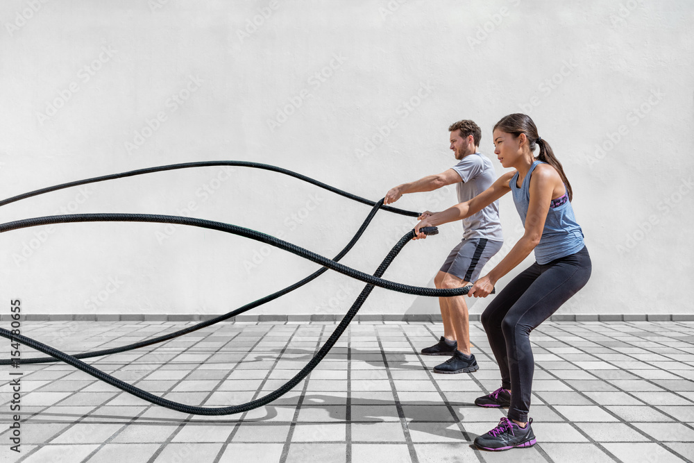 Fitness people exercising with battle ropes at gym. Woman and man