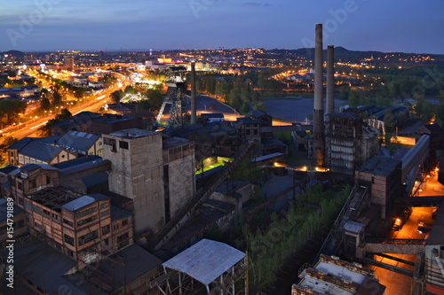 Abandoned ironworks factory in the dark with a shining city in the background © msvantny