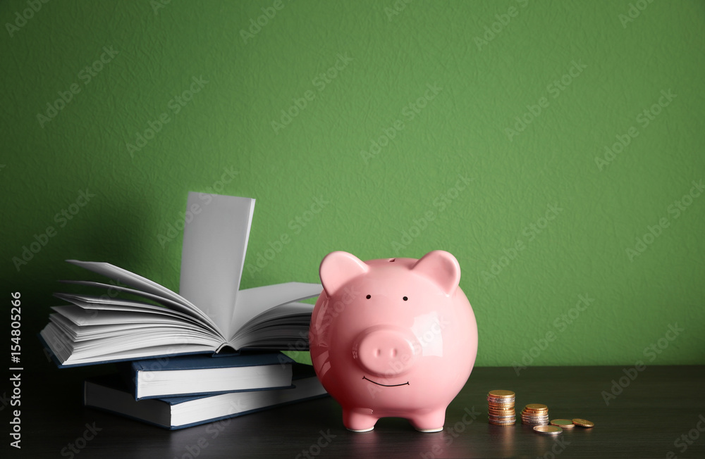 Ceramic piggy bank with books and coins on green background Ceramic piggy bank with books and coins on green background