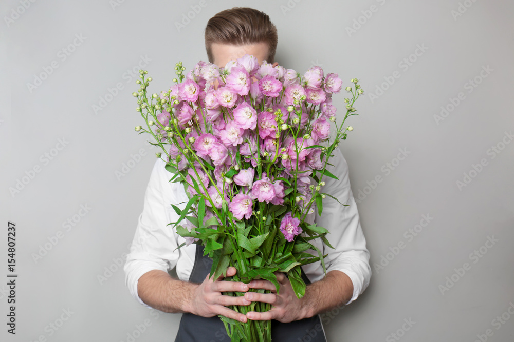 Young florist hiding behind beautiful bouquet on grey background Young florist hiding behind beautiful bouquet on grey background