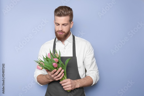 Young handsome florist with beautiful bouquet on blue background