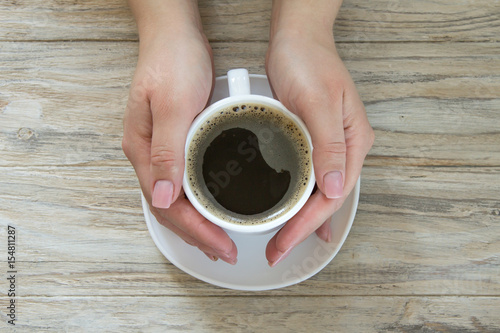 Cup of black aroma coffee in womans hand on wooden background