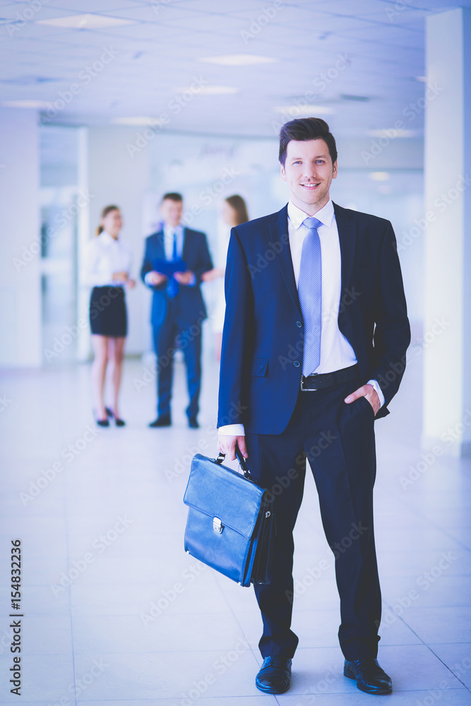 Portrait of young businessman in office with colleagues in the background Portrait of young businessman in office with colleagues in the background