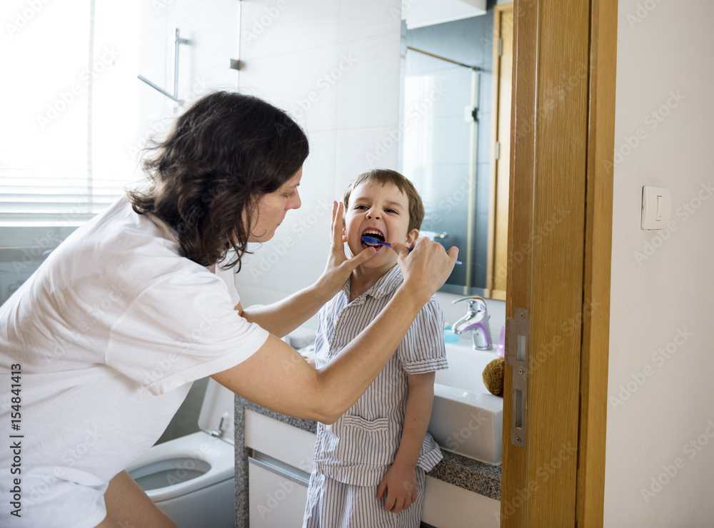 Mother teaching and helping the son how to brush his teeth Mother teaching and helping the son how to brush his teeth