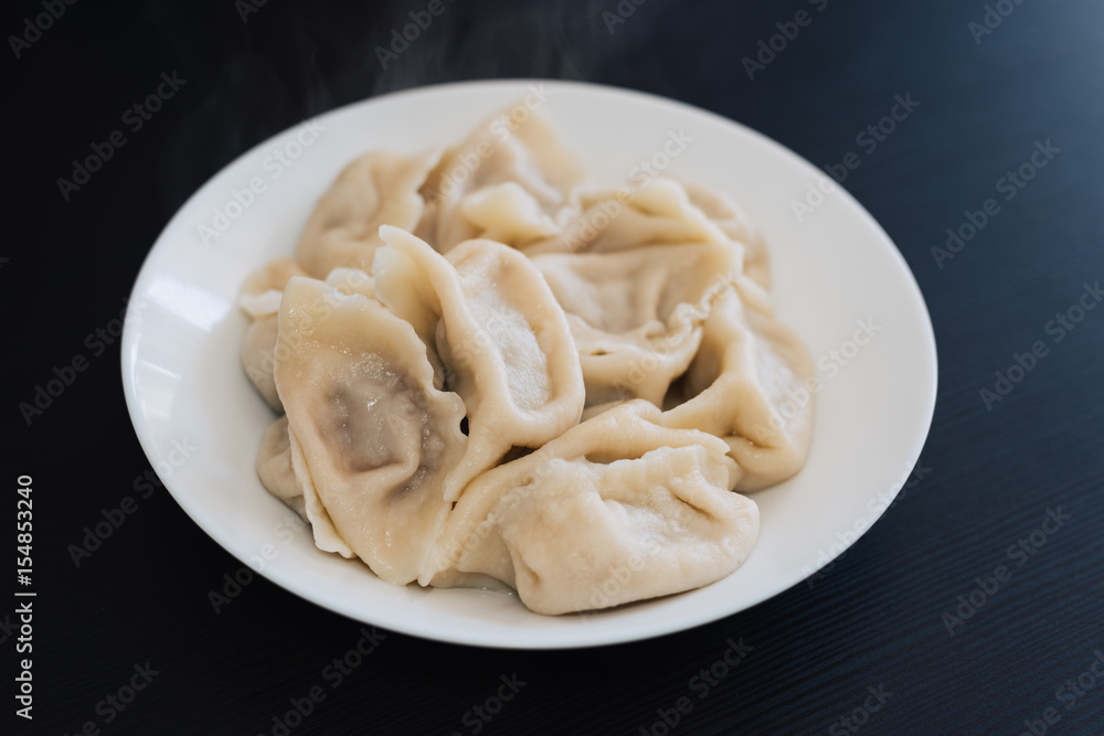 A plate of cooked Chinese dumplings isolated on black background. A must eat for Chinese New Year. A plate of cooked Chinese dumplings isolated on black background. A must eat for Chinese New Year.