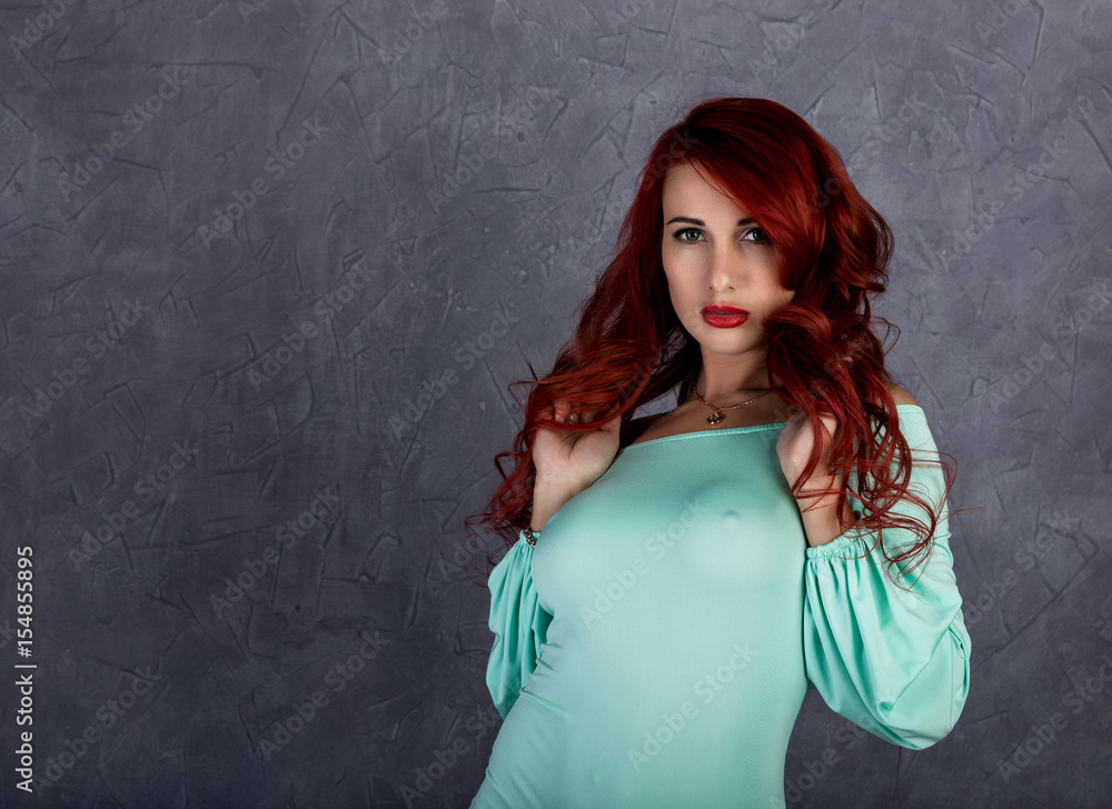 sexy beautiful redhead young woman with big boobs in a turquoise dress on a  gray background Stock Photo | Adobe Stock