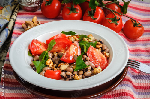 Close up of healthy and delicious salad with ripe tomatoes bean walnuts served in a plate.
