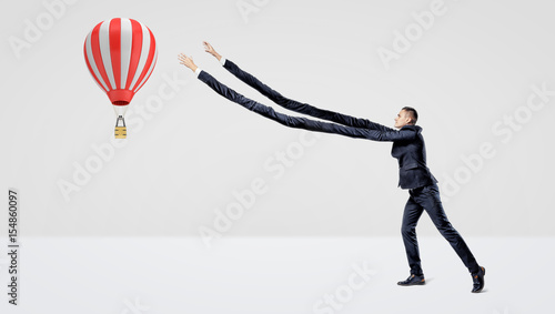Quadro em tela A businessman in side view trying to catch a large flying hot air balloon with his extra-long arms