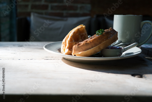 2 pieces of waffle with a white cup of coffee on the wooden table - dark tone