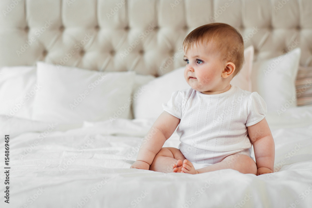 Baby girl in white clothets sit on the bed 