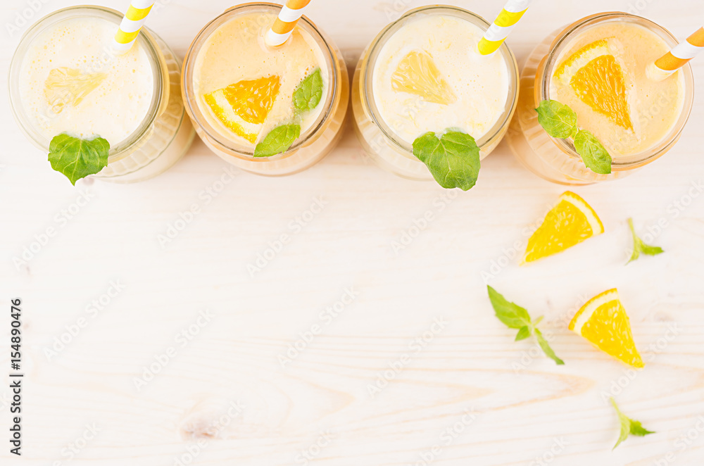 Freshly blended orange and yellow lemon smoothie in glass jars with straw, mint leaf, slices orange and lemon, top view. White wooden board background, copy space. Freshly blended orange and yellow lemon smoothie in glass jars with straw, mint leaf, slices orange and lemon, top view. White wooden board background, copy space.