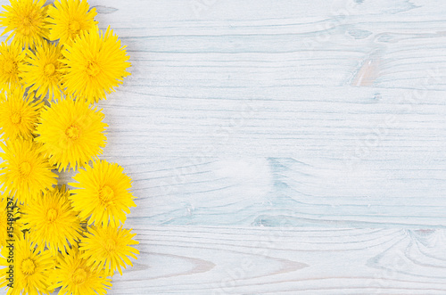 Fototapeta Naklejka Na Ścianę i Meble -  Yellow dandelion flowers as decorative border on light blue wooden board. Copy space, top view.