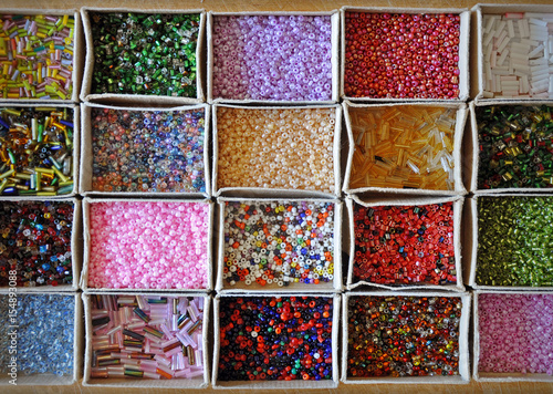 Many kinds of beads of different colors and shapes in cardboard boxes. Background, top view.