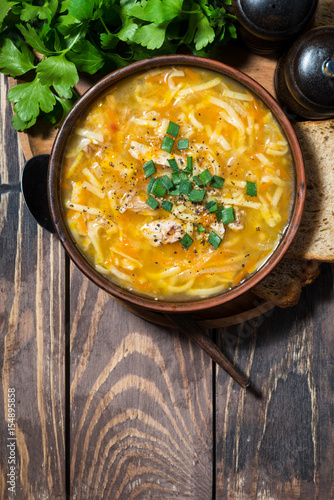 chicken soup with egg noodles on wooden background, vertical top view