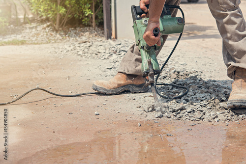 Builder worker with pneumatic hammer drill equipment breaking concrete floor at construction site